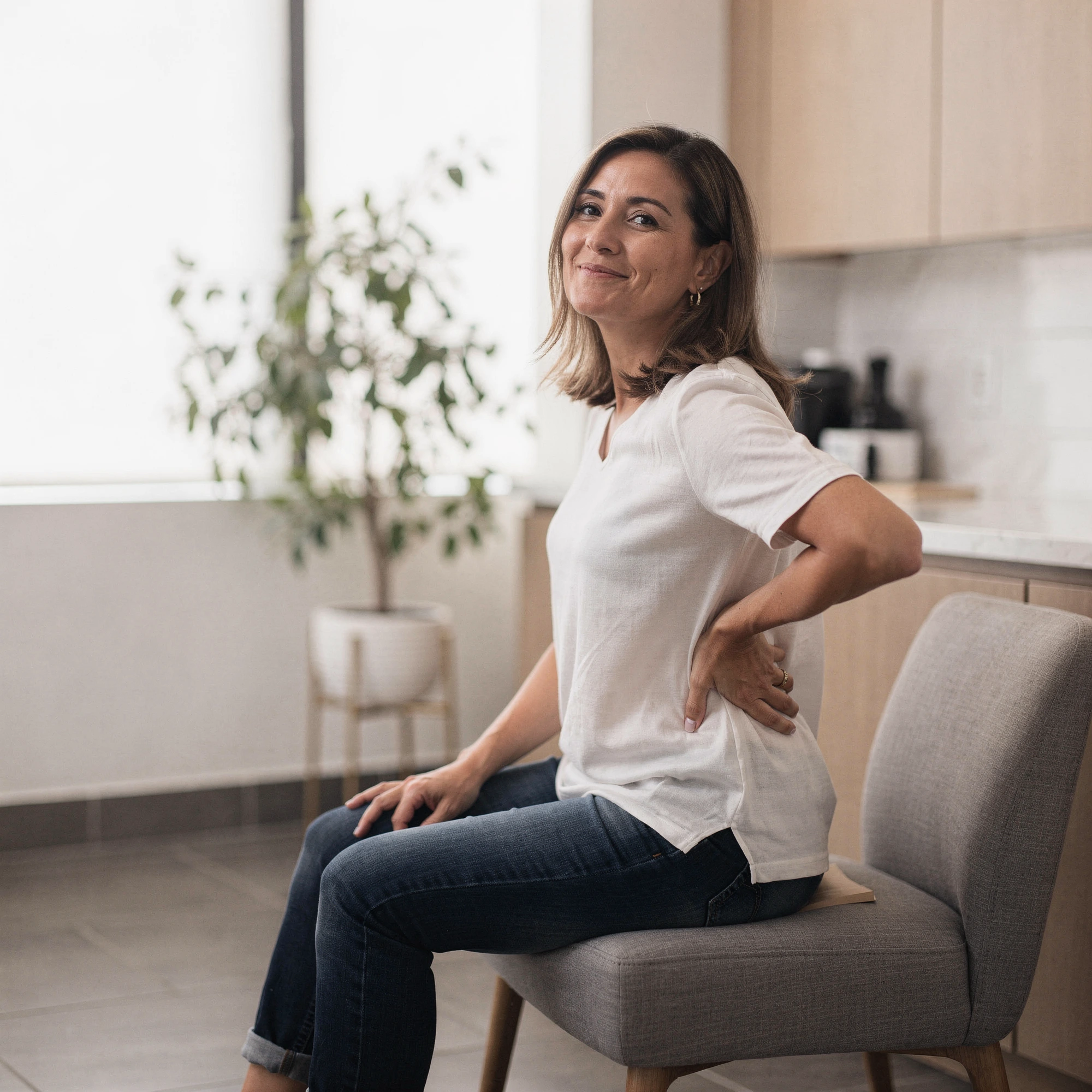 Woman sitting on a chair holding her lower back, indicating back pain